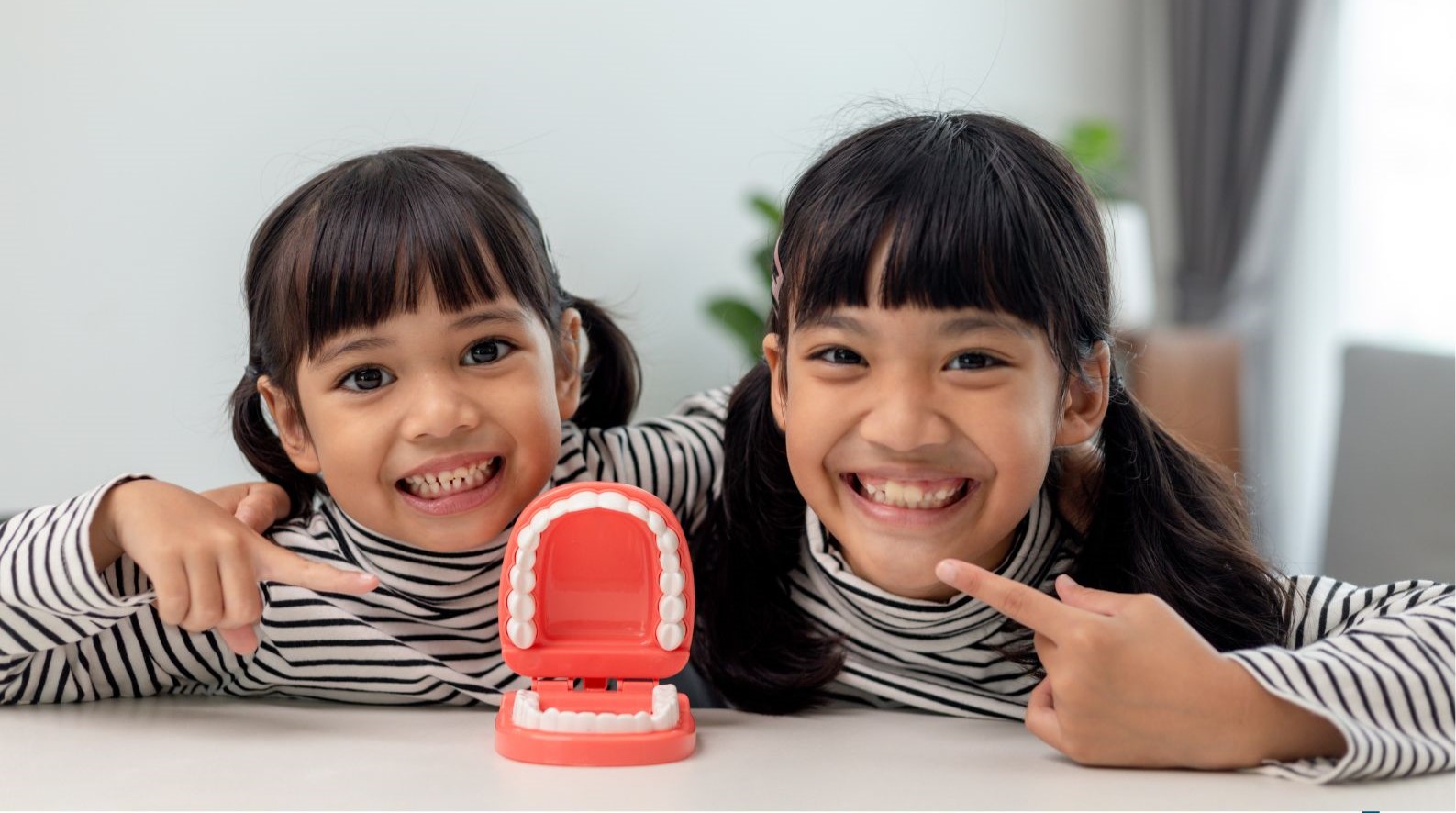 Two children smiling and pointing at their teeth behind a clicky teeth toy