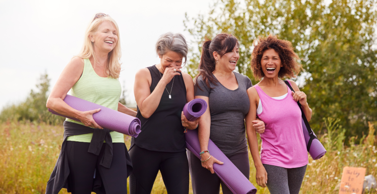 Four women walking and laughing, carrying exercise mats