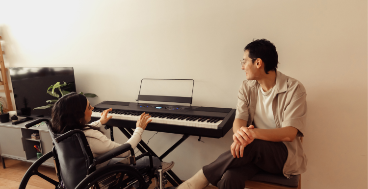 young woman in a wheelchair playing the keyboard while a man sitting on a chair chats to her