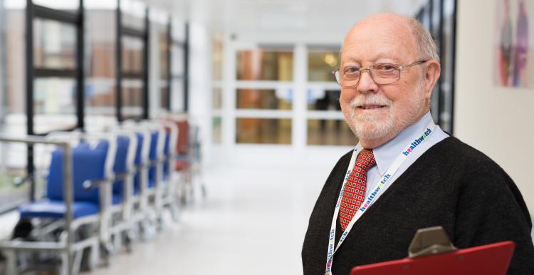 Man in a hospital corridor holding a clipboard