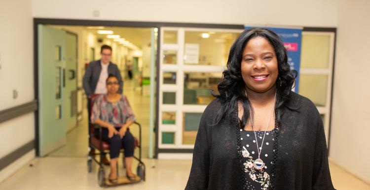 lady standing in a hospital corridor, lady in a wheelchair in the background