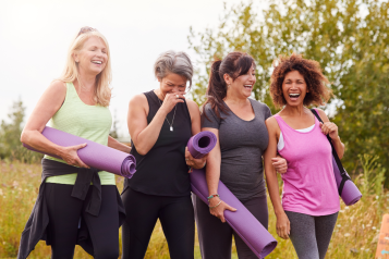 Four women walking and laughing, carrying exercise mats