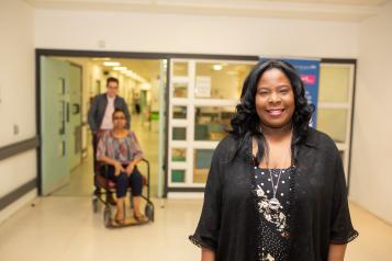 lady standing in a hospital corridor, lady in a wheelchair in the background